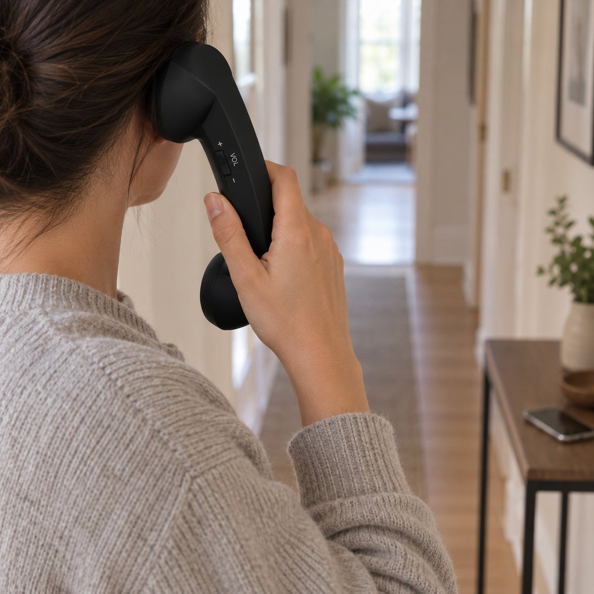Walking down a hallway on a call with the Black Novapix Bluetooth Retro Handset, phone left on the side table