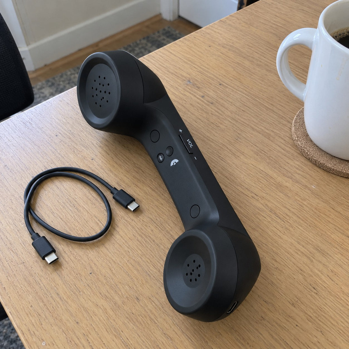 Customer photo: Black Novapix Bluetooth Retro Handset on a desk with its charging cable and a coffee