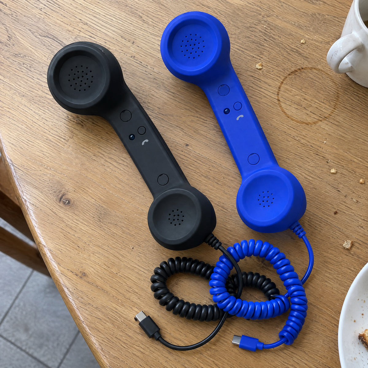 Black and blue retro handsets side by side on a wooden table, each with a coiled cord ending in a USB-C plug